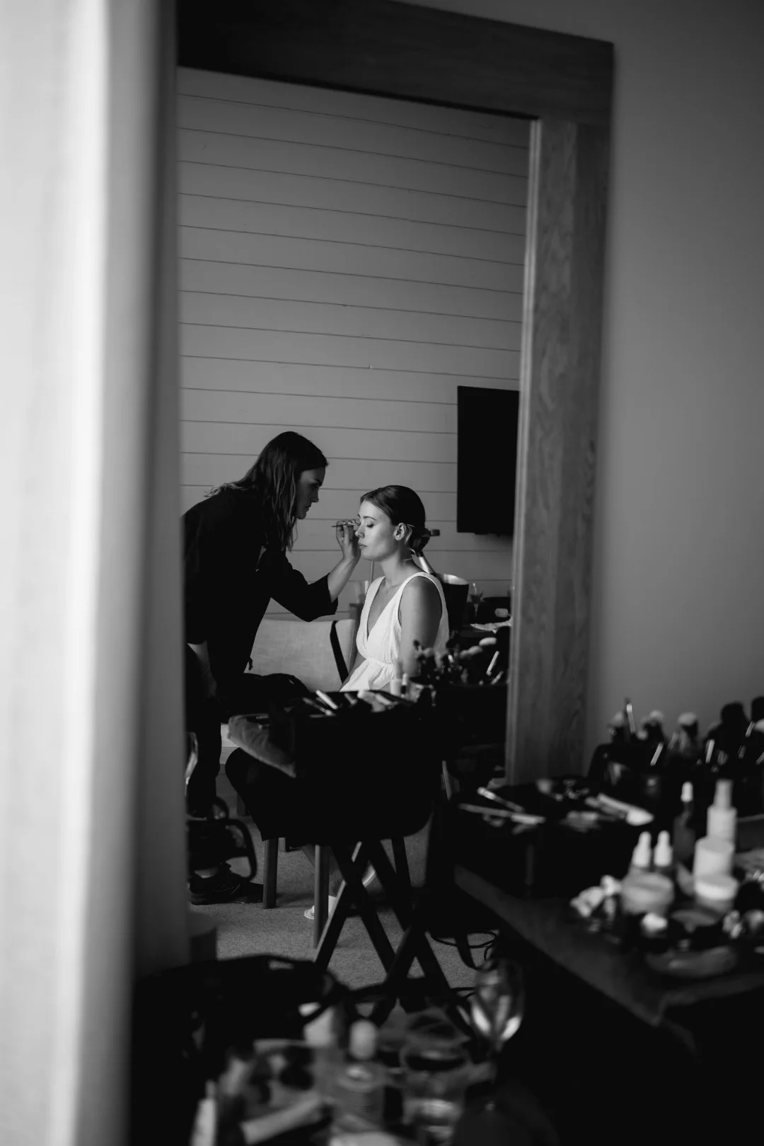 Lovina doing a bride's makeup, seen through a doorway, black and white