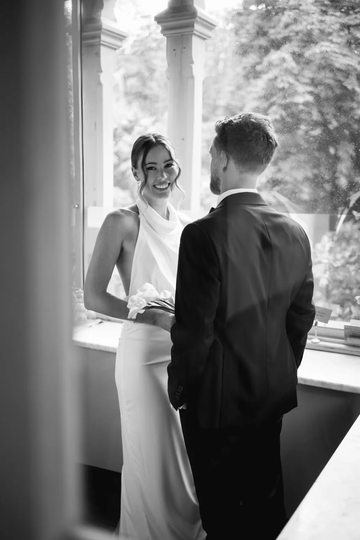 A bride and groom by a window, black and white